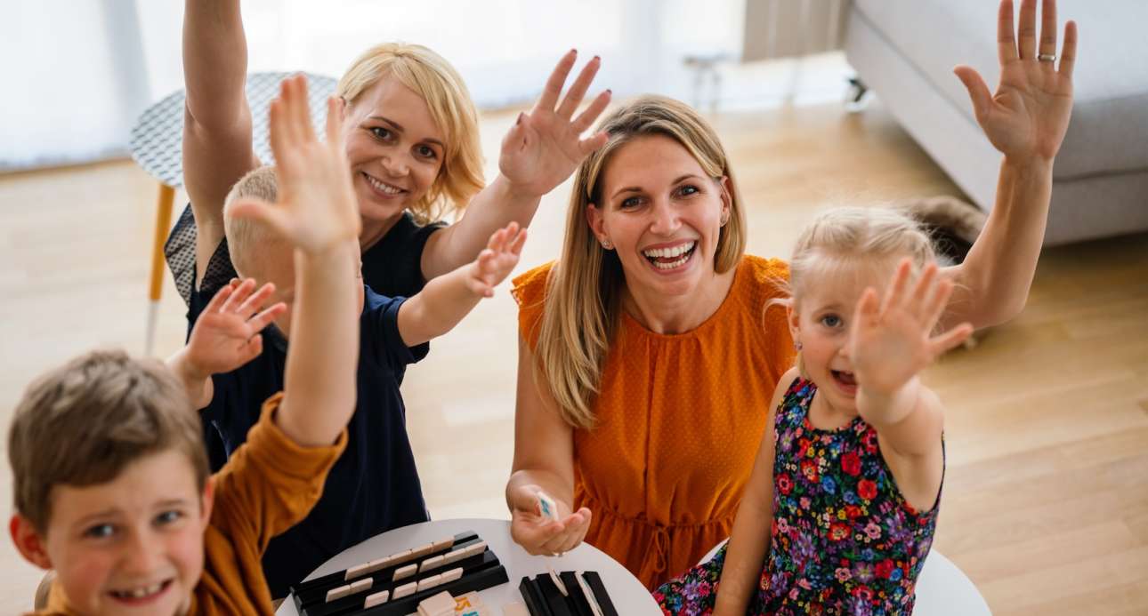 Family at the table playing board game with children. Lesbian couple, nursery, childhood concept.